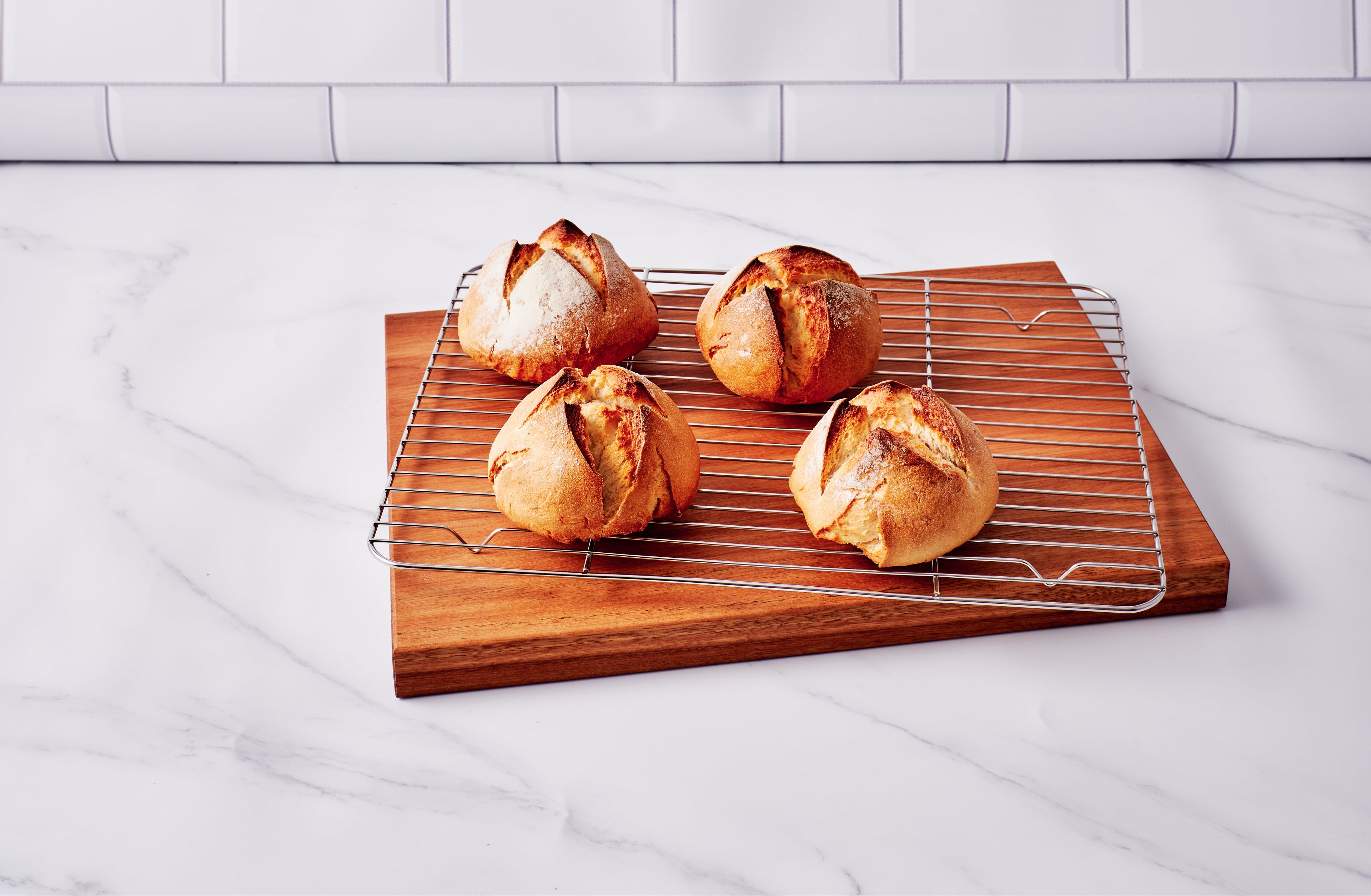 Baked bread loaves on a cooling rack with a wooden board against a tiled wall background